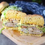 Chicken or Turkey Taco Burger cut in half on wood plate. The burger has smokey taco seasonings, cilantro, and scallions. Then on top are melty cheese, guacamole, lettuce, tomato, and chipotle mayonnaise!
