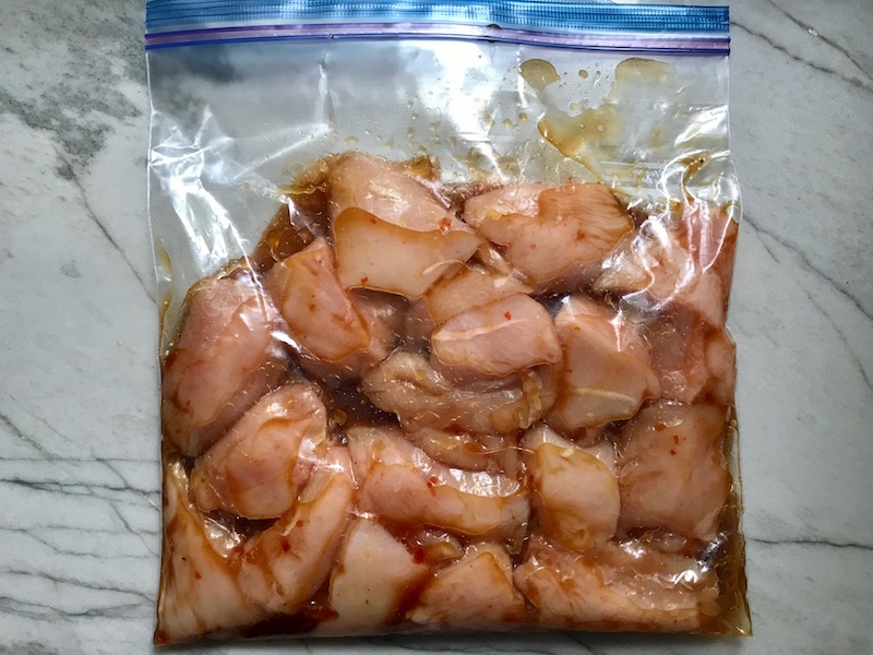 Raw Chicken breast kabob pieces marinating in large storage bag for Sweet and Sour sauce Chicken Kabobs with pineapple, onion, and red pepper.