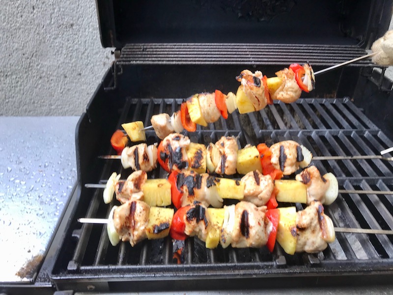 Flipping over Sweet and Sour Chicken Kabobs with pineapple, onion, and red pepper on gas grill..
