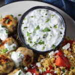 Tzatziki sauce in a bowl on plate with greek meatballs.This is a delicious and easy Tzatziki Recipe with cool and creamy yogurt, fresh cucumber, lime zest, garlic, and scallion.