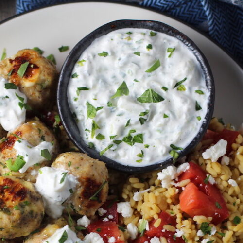 Tzatziki sauce in a bowl on plate with greek meatballs.This is a delicious and easy Tzatziki Recipe with cool and creamy yogurt, fresh cucumber, lime zest, garlic, and scallion.