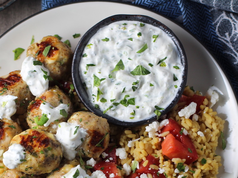 Tzatziki sauce in a bowl on plate with greek meatballs.This is a delicious and easy Tzatziki Recipe with cool and creamy yogurt, fresh cucumber, lime zest, garlic, and scallion.