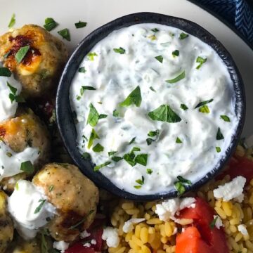 Tzatziki sauce in a bowl on plate with greek meatballs.This is a delicious and easy Tzatziki Recipe with cool and creamy yogurt, fresh cucumber, lime zest, garlic, and scallion.