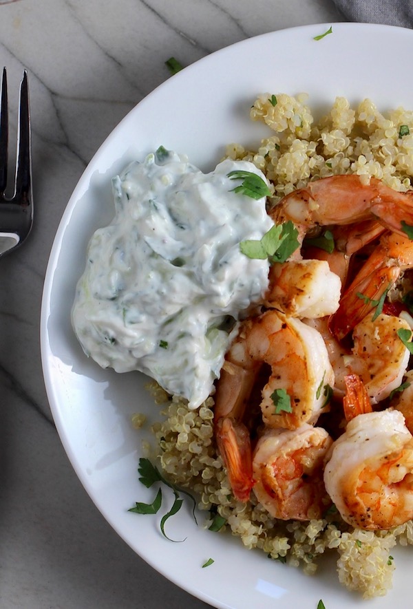 Tzatziki sauce on a plate next to shrimp over quinoa. This is a delicious and easy Tzatziki Recipe with cool and creamy yogurt, fresh cucumber, lime zest, garlic, and scallion.