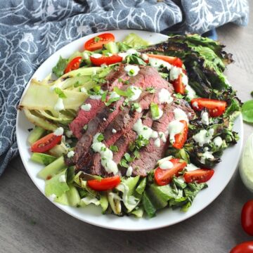 Sliced Grilled Flank Steak Salad Recipe on plate with grilled romaine, halved grape tomatoes, and creamy basil yogurt dressing.