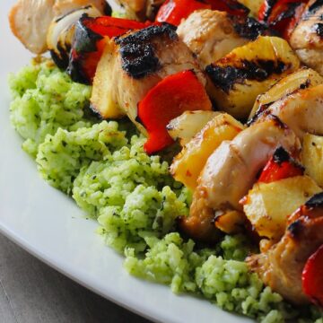 Green Rice on platter with chicken kabobs on top. This Recipe takes white rice from plain to amazing with just 5 ingredients. Filled with herbs and spinach, it has the perfect herby flavor.