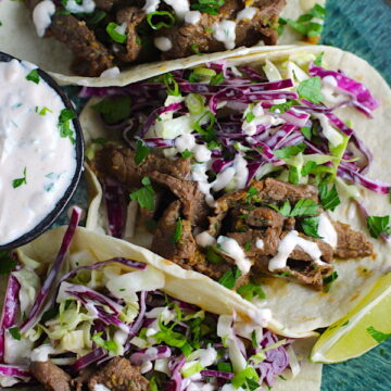 Korean Bulgogi Sauce Beef Tacos on a plate with flavorful Korean beef, crunchy Sesame Cabbage Slaw and a creamy, cool, Cilantro Lime Sriracha sauce!
