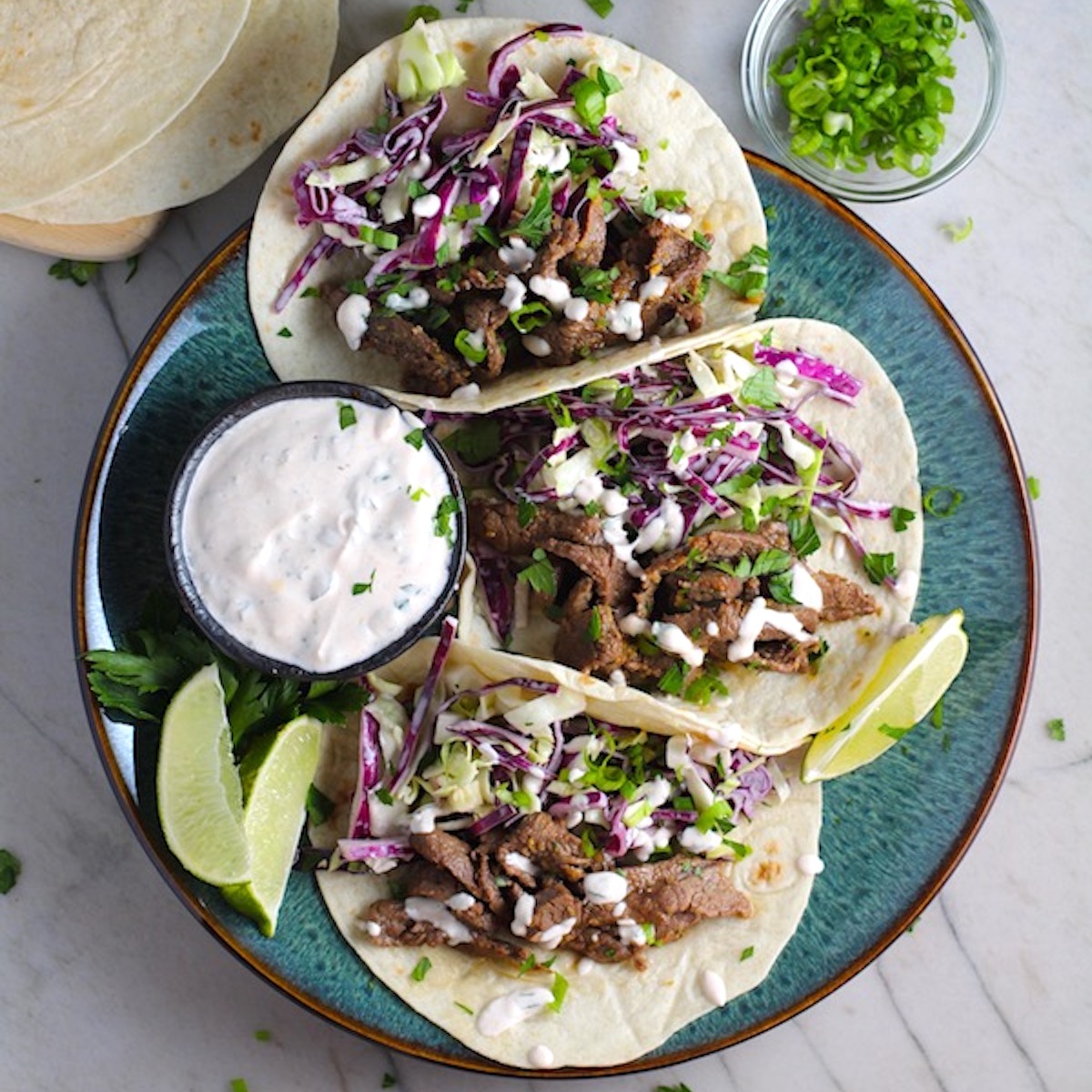 Korean Beef Tacos on a plate with flavorful Korean beef, crunchy Sesame Cabbage Slaw and a creamy, cool, Cilantro Lime Sriracha sauce!
