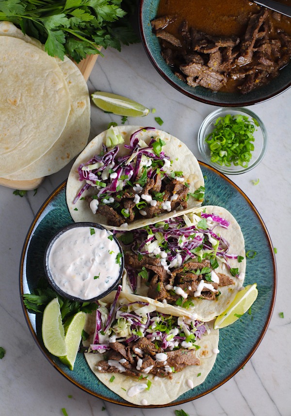 Korean Beef Tacos on a plate with flavorful Korean beef, crunchy Sesame Cabbage Slaw and a creamy, cool, Cilantro Lime Sriracha sauce!