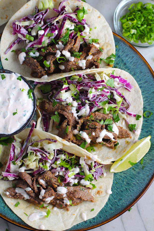 Korean Beef Tacos on a plate with flavorful Korean beef, crunchy Sesame Cabbage Slaw and a creamy, cool, Cilantro Lime Sriracha sauce!