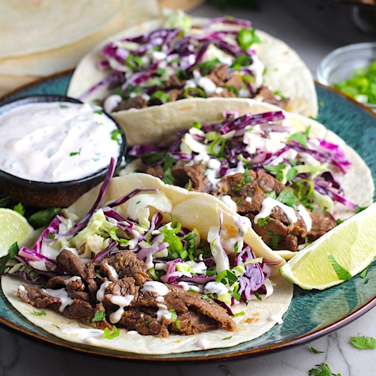 Korean Beef Tacos on a plate with flavorful Korean beef, crunchy Sesame Cabbage Slaw and a creamy, cool, Cilantro Lime Sriracha sauce!