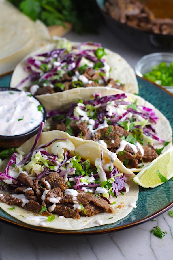 Korean Beef Tacos on a plate with flavorful Korean beef, crunchy Sesame Cabbage Slaw and a creamy, cool, Cilantro Lime Sriracha sauce!