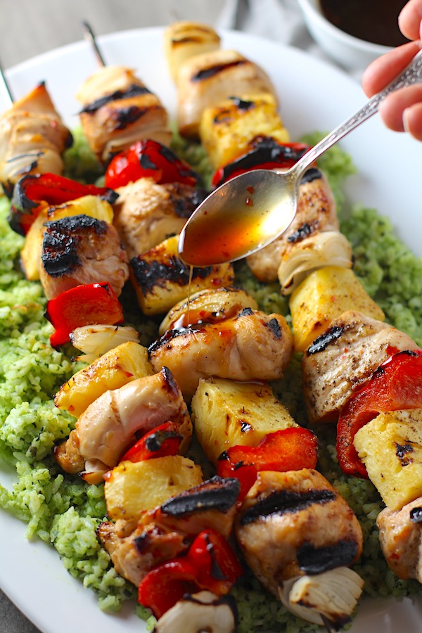 Spoon drizzling Sweet and Sour sauce over Chicken Kabobs with pineapple, onion, and red pepper over Green Rice with basil, chives, and spinach.