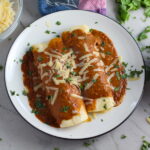 Chicken Mole Enchiladas, on a plate with cheese and cilantro on top. They are easy to make and delicious! The Mole sauce has unsweetened chocolate, tomatoes, green chilis, garlic, adobo sauce, and spices blend harmoniously!