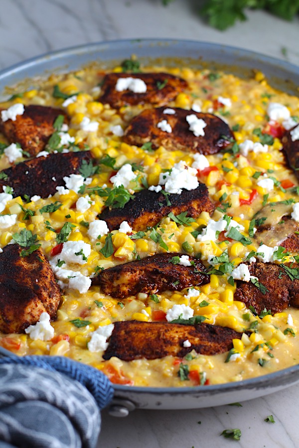 Creamy Corn and Blackened Chicken with feta and cilantro on top in a pan.