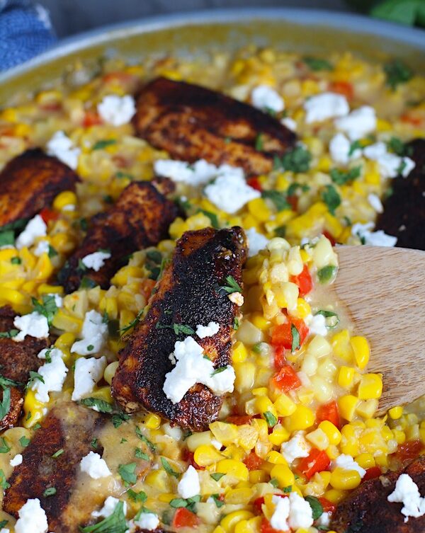 Creamy Corn and Blackened Chicken with feta and cilantro on top in a pan with spatula scooping.