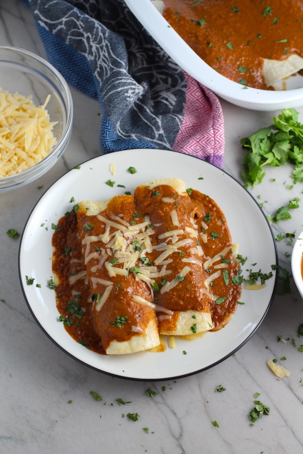 Chicken Enchiladas Mole Sauce Recipe on a plate with cheese and cilantro on top. They are easy to make and delicious! The Mole sauce has unsweetened chocolate, tomatoes, green chilis, garlic, adobo sauce, and spices blend harmoniously!