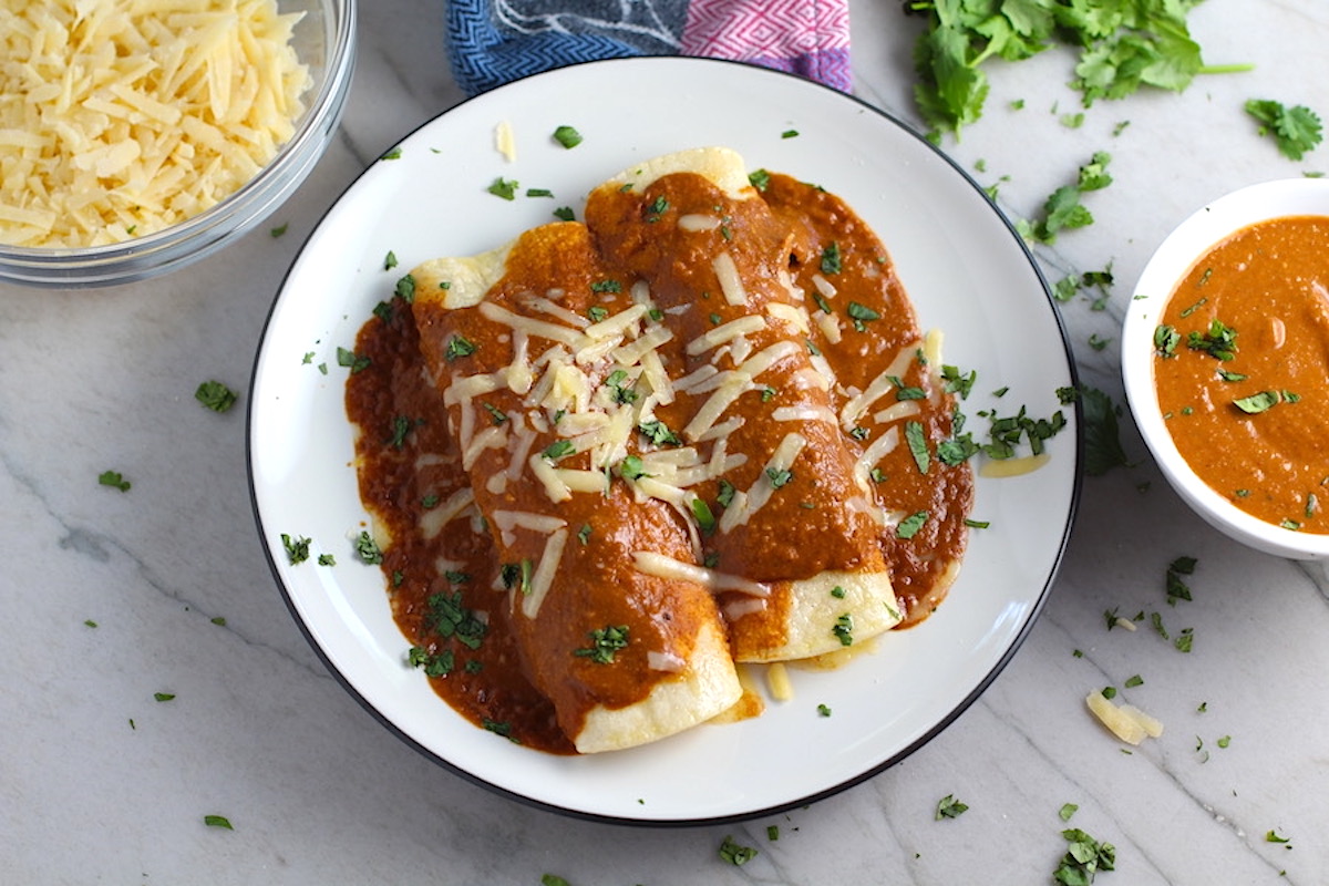 Chicken Mole sauce recipe Enchiladas on a plate with cheese and cilantro on top. They are easy to make and delicious! The Mole sauce has unsweetened chocolate, tomatoes, green chilis, garlic, adobo sauce, and spices blend harmoniously!