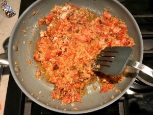 Spatula mixing quinoa, chorizo, tomato filling in pan for Stuffed Tomatoes with chorizo, quinoa, parmesan cheese, chives, garlic, and oregano.