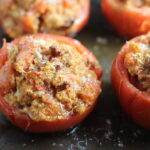 Stuffed Tomatoes on sheet pan on counter with chorizo, quinoa, parmesan cheese, chives, garlic, and oregano are simply divine! 