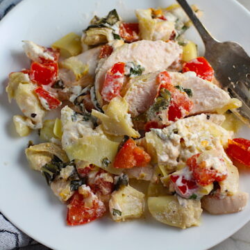 Chicken Artichoke Bake with Tomatoes and Goat Cheese on a plate with fork. It's a creamy, tangy, sweet, savory, mouth watering easy dinner that you can prep ahead!