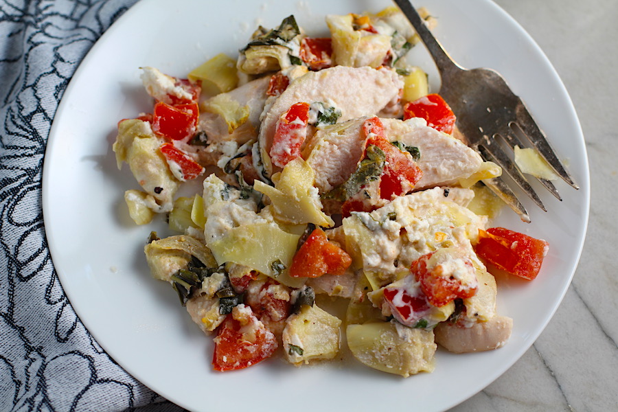 Chicken Artichoke Bake with Tomatoes and Goat Cheese on a plate with fork. It's a creamy, tangy, sweet, savory, mouth watering easy dinner that you can prep ahead!