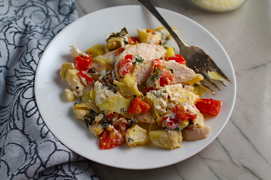 Chicken Artichoke Bake with Tomatoes and Goat Cheese on a plate with fork. It's a creamy, tangy, sweet, savory, mouth watering easy dinner that you can prep ahead!