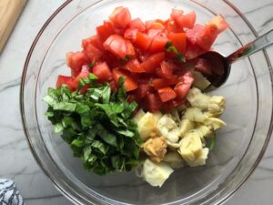 Cut artichoke hearts, tomatoes, and basil in bowl for Chicken Artichoke Bake with Tomatoes and Goat Cheese. It's a creamy, tangy, sweet, savory, mouth watering easy dinner that you can prep ahead!
