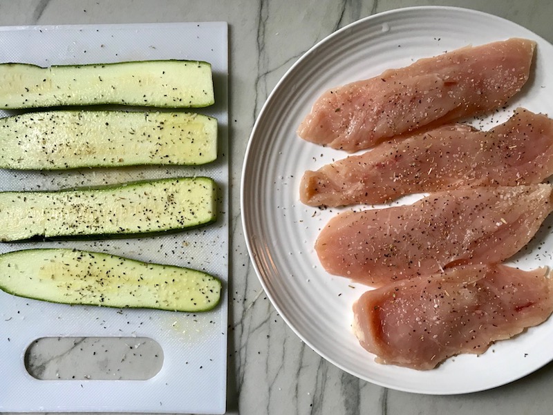 Raw zucchini slices and chicken breasts seasoned for Chicken Parmesan Pasta Bake. It cooks entirely in one casserole dish, including the pasta! Shell pasta in flavorful, tangy tomato sauce is topped with zucchini, chicken, mozzarella, parm, and crunchy breadcrumb topping.