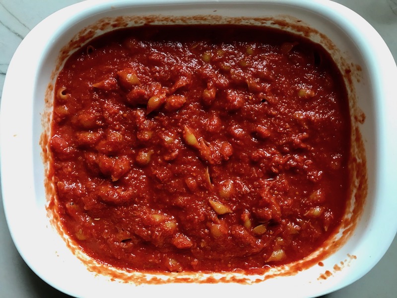 Pasta and tomato sauce in casserole dish for Chicken Parmesan Pasta Bake. It cooks entirely in one casserole dish, including the pasta! Shell pasta in flavorful, tangy tomato sauce is topped with zucchini, chicken, mozzarella, parm, and crunchy breadcrumb topping.