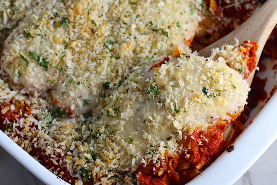 Chicken Parmesan Pasta Bake in the pan with spatula scooping. It cooks entirely in one casserole dish, including the pasta! Shell pasta in flavorful, tangy tomato sauce is topped with zucchini, chicken, mozzarella, parm, and crunchy breadcrumb topping.