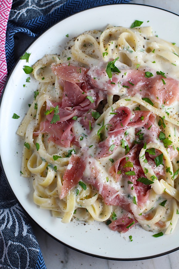 Easy Fettuccine Alfredo with Prosciutto on a plate with fork scooping pasta. It's a creamy but lighter recipe without the heavy cream or butter, but still delicious!