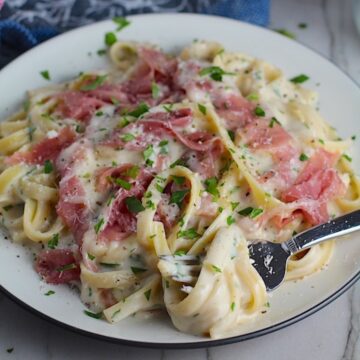Fettuccine Lower Fat Alfredo Sauce Recipe with Prosciutto on a plate with fork scooping pasta. It's a creamy but lighter recipe without the heavy cream or butter, but still delicious!