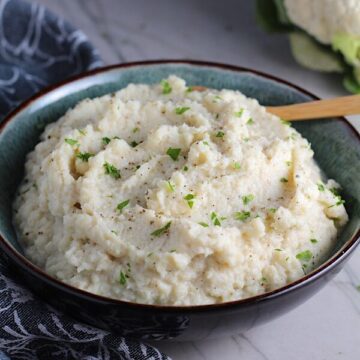 Mashed Roasted Cauliflower in a bowl with spoon. The texture is perfectly creamy and along with the flavor, mimics mashed potatoes.