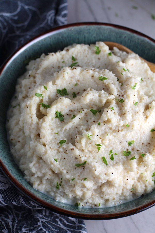 Roasted Garlic Cauliflower Mash in a bowl with spoon. The texture is perfectly creamy and along with the flavor, mimics mashed potatoes.