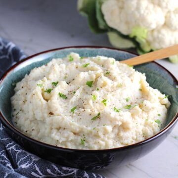 Mashed Roasted Cauliflower in a bowl with spoon. The texture is perfectly creamy and along with the flavor, mimics mashed potatoes.