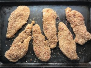 Raw chicken coated in bacon breadcrumbs on pan for Oven Fried Chicken Breast. The chicken is coated with Bacon Crumbs and Honey and it's healthier because it's baked, not fried, but still gives you all of the crispy, crunchy goodness! It also gives you sweet and salty crunch with the addition of honey and bacon!