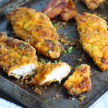 Oven Fried Chicken Breast cut on pan with bacon in background. The chicken is coated with Bacon Crumbs and Honey and it's healthier because it's baked, not fried, but still gives you all of the crispy, crunchy goodness! It also gives you sweet and salty crunch with the addition of honey and bacon!