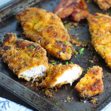 cut on pan with bacon in background. The chicken is coated with Bacon Crumbs and Honey and it's healthier because it's baked, not fried, but still gives you all of the crispy, crunchy goodness!  It also gives you sweet and salty crunch with the addition of honey and bacon!