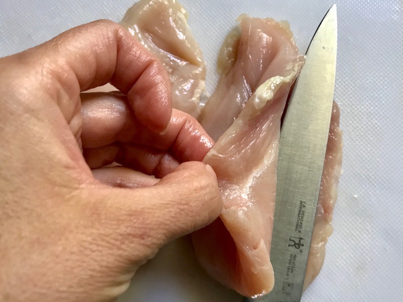Knife slicing raw chicken for One Pot Chicken Cordon Bleu Bake. On the bottom you get flavorful rice topped with chicken, salty ham, nutty and melty swiss cheese, and a crunchy breadcrumb topping!