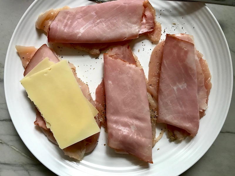 Sliced raw chicken with deli ham and slice of cheese on top for One Pot Chicken Cordon Bleu Bake. On the bottom you get flavorful rice topped with chicken, salty ham, nutty and melty swiss cheese, and a crunchy breadcrumb topping!