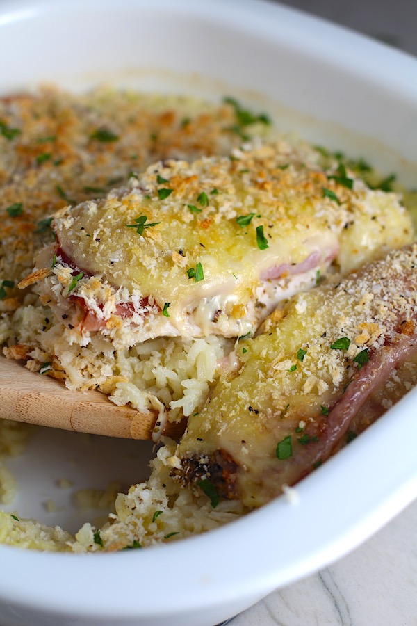 Spatula scooping out a piece of the One Pot Chicken Cordon Bleu and Rice Casserole in casserole dish. On the bottom you get flavorful rice topped with chicken, salty ham, nutty and melty swiss cheese, and a crunchy breadcrumb topping!