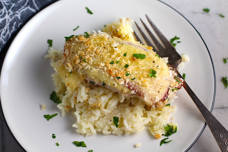 Piece of One Pot Chicken Cordon Bleu and Rice Casserole on a plate with fork. On the bottom you get flavorful rice topped with chicken, salty ham, nutty and melty swiss cheese, and a crunchy breadcrumb topping!
