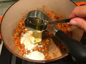 Flour being added to carrots and onions in pot for Creamy Chicken Sausage and Tortellini Soup. It's silky and creamy with onions, garlic, Chicken sausage, and zucchini bring so much flavor and texture. The tortellini give that delicious salty, creamy, hearty bite!