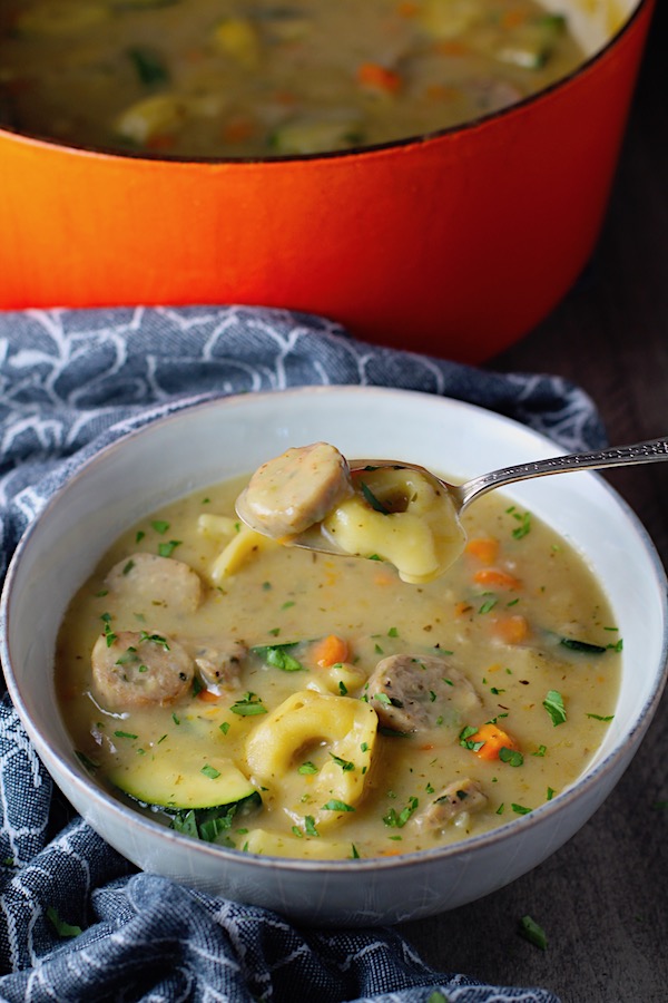 Creamy Chicken Sausage and Tortellini Soup in a bowl with spoonful of soup above bowl. It's silky and creamy with onions, garlic, Chicken sausage, and zucchini bring so much flavor and texture. The tortellini give that delicious salty, creamy, hearty bite!