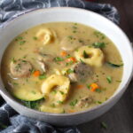 Creamy Chicken Sausage and Tortellini Soup in a bowl on table. It's silky and creamy with onions, garlic, Chicken sausage, and zucchini bring so much flavor and texture.  The tortellini give that delicious salty, creamy, hearty bite! 