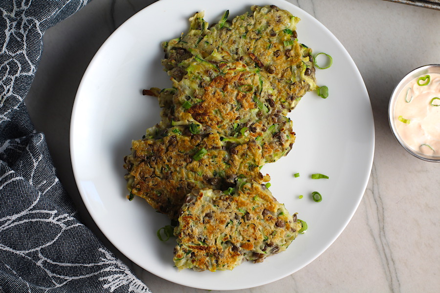 Lentil and Zucchini Cakes on a plate with Sriracha sauce on the side. They have a crispy outside and soft inside and are perfect for an easy dinner! The flavors are simple but perfect with parmesan, oregano, scallions, lentils, and zucchini.