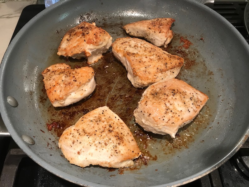 Cooked chicken in pan for Smothered Chicken with Bacon, and Tomatoes. The chicken is smothered in a thickened sauce infused with smokey and salty bacon flavor. Cherry tomatoes give a sweet and tangy pop.