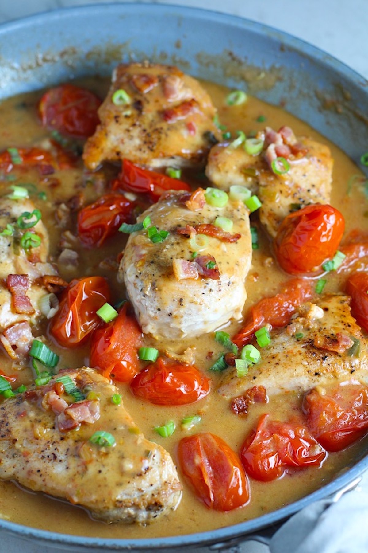 Creamy Bacon Chicken with Tomatoes in a pan. The chicken is smothered in a thickened sauce infused with smokey and salty bacon flavor. Cherry tomatoes give a sweet and tangy pop.