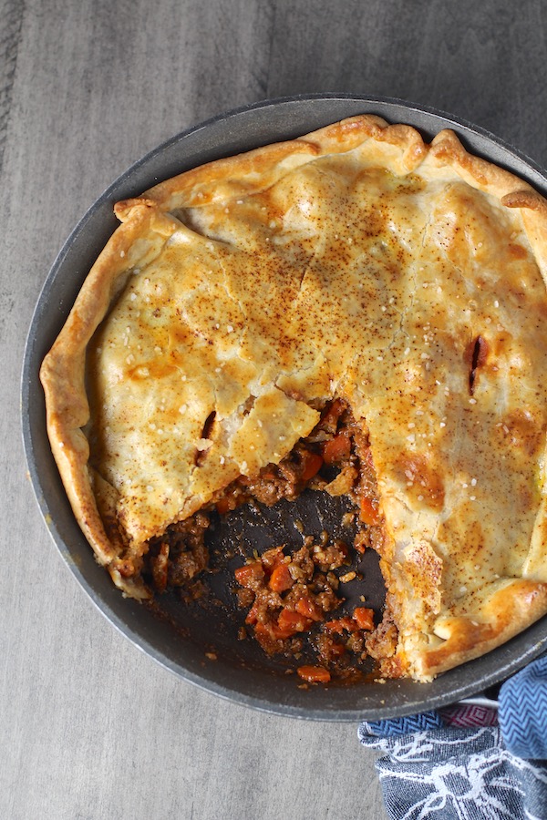Flaky Empanada Pie with Ground Beef Recipe in a skillet with a piece out on counter. It has a perfect flaky, buttery pastry on the outside with a savory, smokey, salty ground beef filling. The best part is that everything cooks in one skillet!